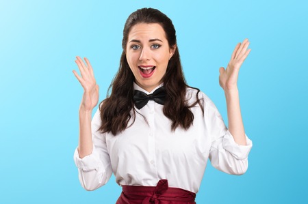 Young beautiful waitress making surprise gesture on colorful background