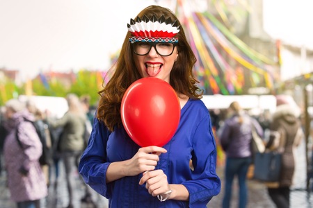 Beautiful young girl holding a red balloon with crazy glasses on unfocused backgroundの写真素材