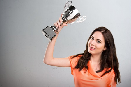 Beautiful young girl holding a trophy on grey backgroundの写真素材