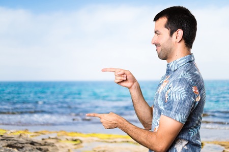 Handsome man with flower shirt pointing to the lateral at the beachの写真素材
