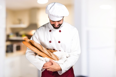 Young baker holding some bread and looking down in the kitchenの写真素材
