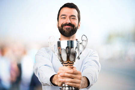 Happy Handsome man with beard holding a trophy on unfocused backgroundの写真素材