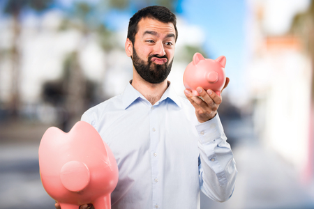 Handsome man with beard holding a piggybank on unfocused backgroundの写真素材