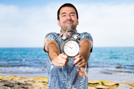 Handsome man with flower shirt holding vintage clock at the beachの写真素材