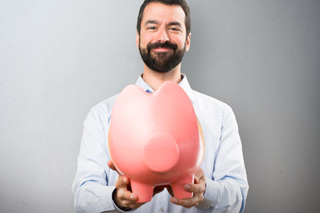 Happy Handsome man with beard holding a piggybank on textured backgroundの写真素材