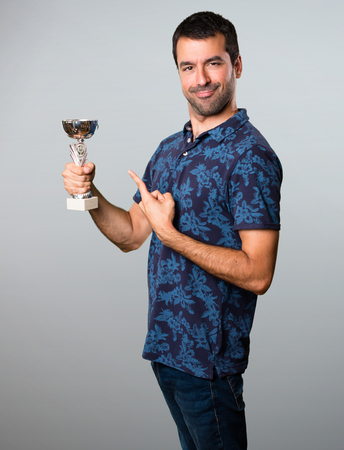 Brunette man holding a trophy on grey backgroundの写真素材