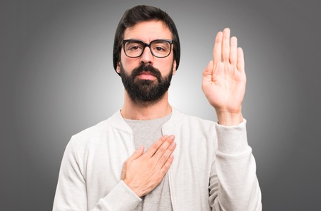 Hipster man making an oath on grey backgroundの写真素材