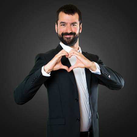 Handsome businessman making a heart with his hands on black backgroundの写真素材