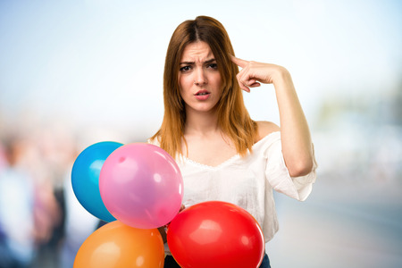 Beautiful young girl holding a balloon and making crazy gesture on unfocused backgroundの写真素材