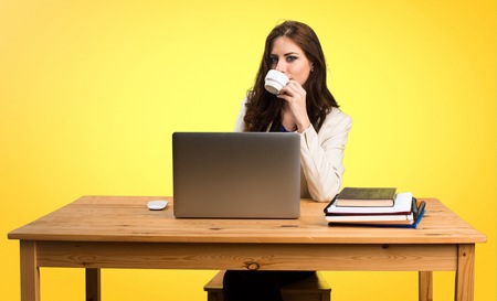 Business woman working with her laptop and holding a cup of coffee on colorful backgroundの写真素材