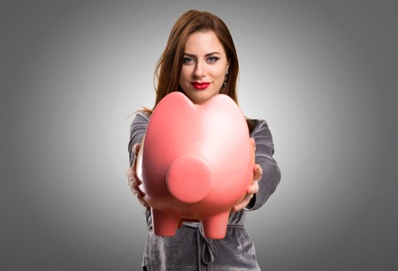 Beautiful young girl holding a piggybank on textured backgroundの写真素材