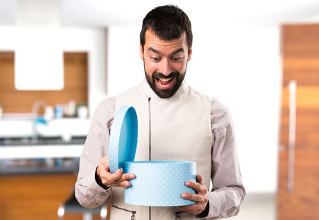 Handsome man with vest holding a gift inside house