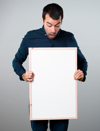Handsome man holding an empty placard on grey backgroundの写真素材