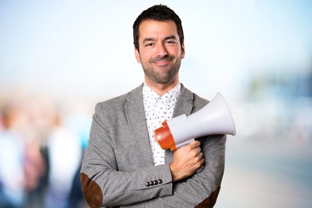 Happy Handsome man holding a megaphone on unfocused backgroundの写真素材