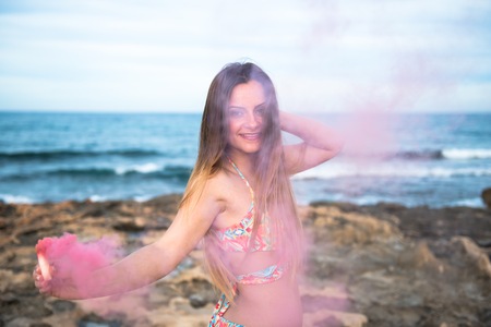Beautiful young girl with smoke bomb in the beach
