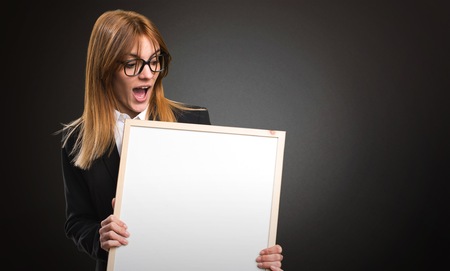 Young business woman holding an empty placard on dark backgroundの写真素材