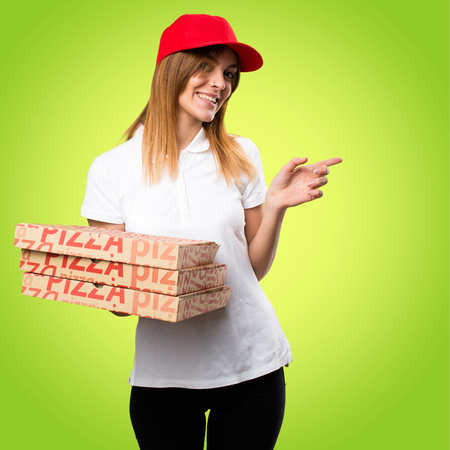 Pizza delivery woman pointing to the lateral on colorful backgroundの写真素材
