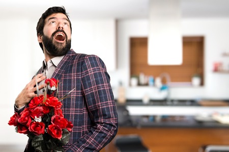 Surprised Well dressed man holding flowers inside houseの写真素材