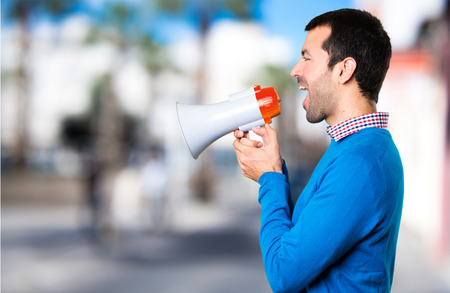 Handsome young man holding a megaphone on unfocused backgroundの写真素材