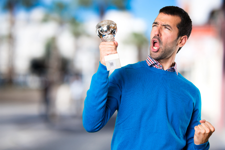Handsome young man holding a trophy on unfocused backgroundの写真素材