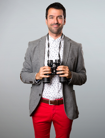 Happy Handsome man with binoculars on grey backgroundの写真素材