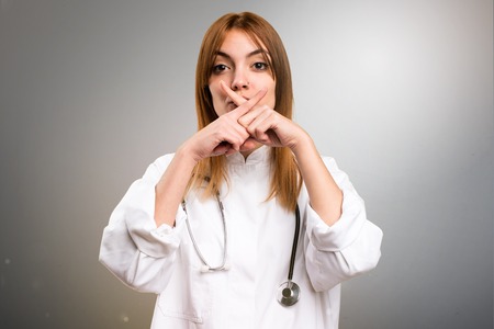 Young doctor woman making silence gesture on grey backgroundの写真素材