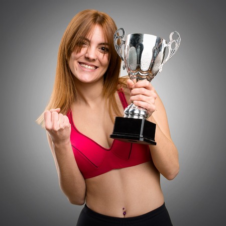 Young sport woman holding a trophy on grey backgroundの写真素材