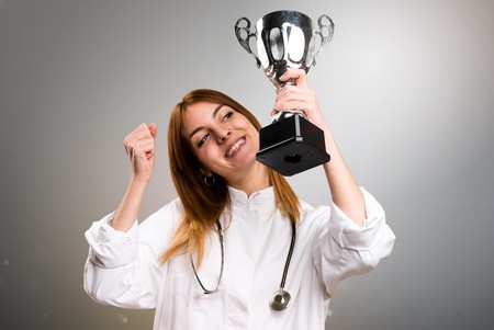 Young doctor woman holding a trophy on grey backgroundの写真素材