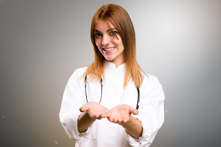 Young doctor woman holding something on grey backgroundの写真素材
