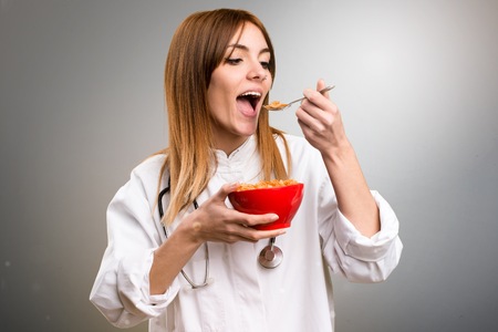 Young doctor woman eating cereals from a bowl on grey background