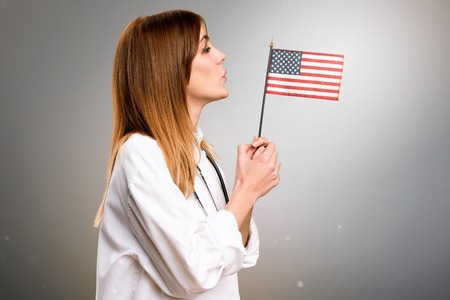Young doctor woman  holding an american flag on grey backgroundの写真素材