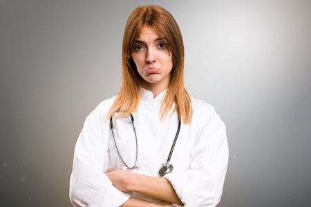 Sad young doctor woman on grey backgroundの写真素材