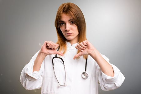 Young doctor woman making bad signal on grey backgroundの写真素材