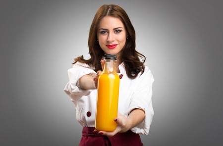 Beautiful chef woman holding a orange juice on grey backgroundの写真素材