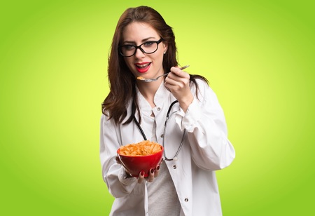 Doctor woman eating cereals from a bowl on green background