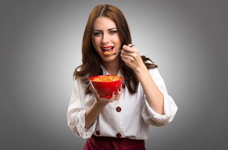 Beautiful chef woman eating cereals from a bowl on grey backgroundの写真素材