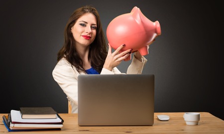 Business woman working with her laptop and holding a piggybank on black backgroundの写真素材