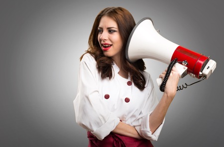 Beautiful chef woman holding a megaphone on grey backgroundの写真素材