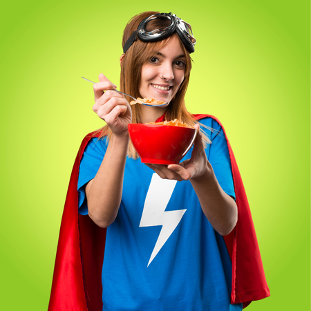 Pretty superhero girl eating cereals from a bowl on colorful backgroundの写真素材