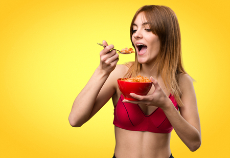 Young sport woman eating cereals from a bowl on colorful backgroundの写真素材
