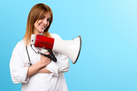 Young doctor woman holding a megaphone on colorful backgroundの写真素材
