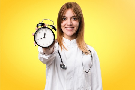 Young doctor woman holding vintage clock on colorful backgroundの写真素材
