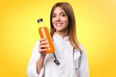 Young doctor woman holding an orange juice on colorful backgroundの写真素材
