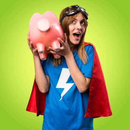 Pretty superhero girl holding a piggybank on colorful backgroundの写真素材