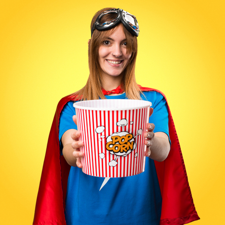 Pretty superhero girl eating popcorns on colorful backgroundの写真素材