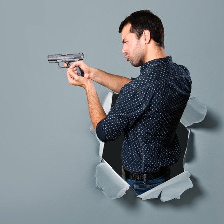 Brunette man shooting with a pistol through a paper holeの写真素材