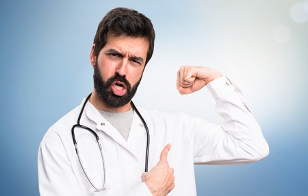 Young doctor making strong gesture on blue backgroundの写真素材