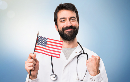 Young doctor holding an american flag on blue backgroundの写真素材