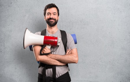 Happy Handsome backpacker holding a megaphone on textured backgroundの写真素材