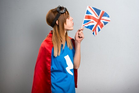 Pretty superhero girl holding an United Kingdom flag on a gray textured backgroundの写真素材